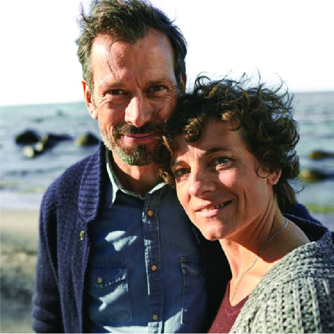 Middle-aged couple smiling together on a beach.