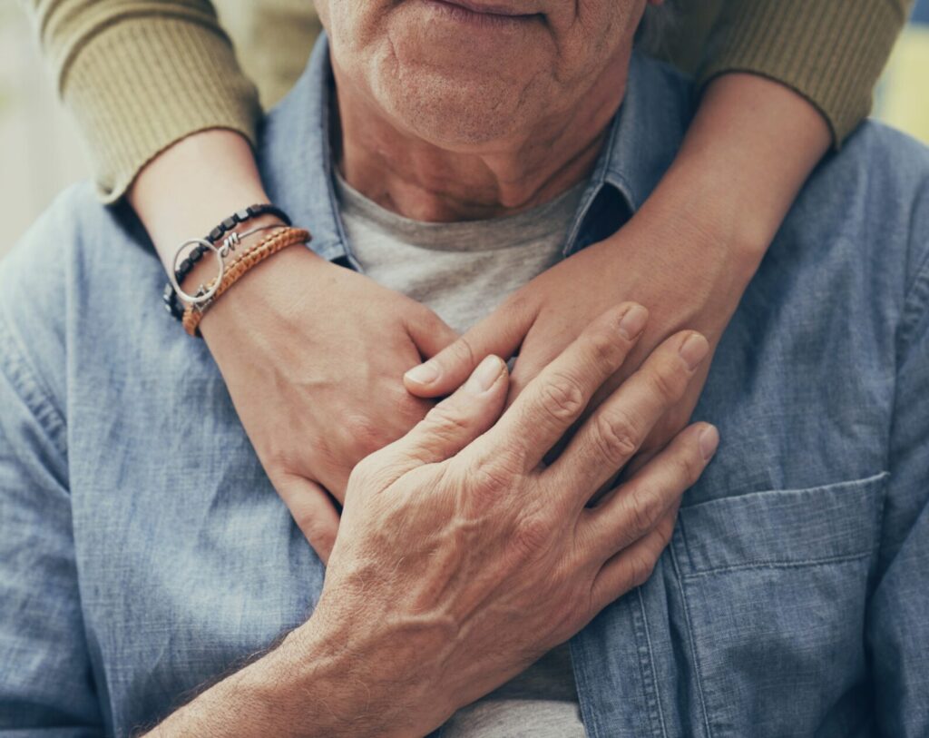Hands resting on the chest of an elderly man, symbolizing comfort and support.