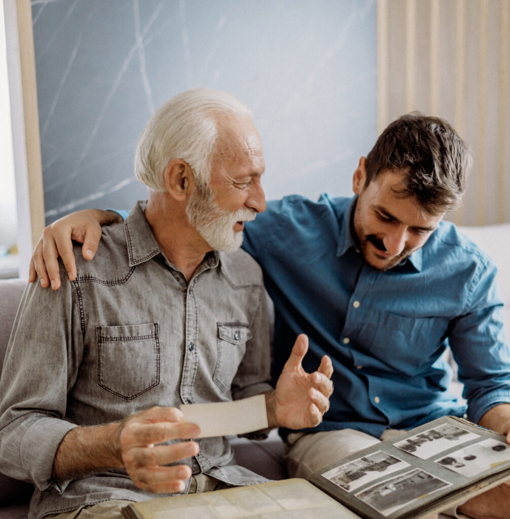 Elderly man and younger man sitting together looking at a photo album.