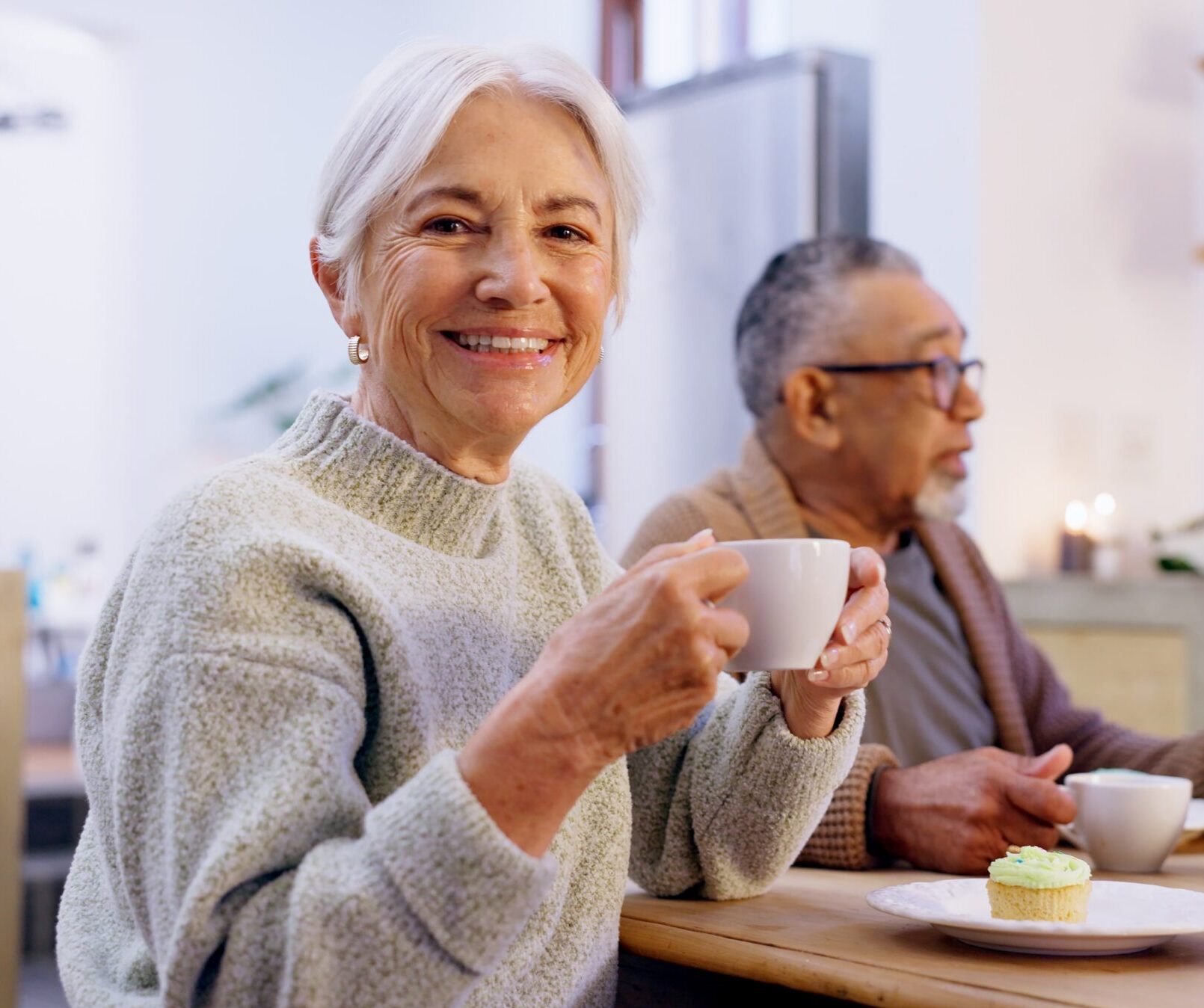 Two elderly people sitting together, one holding a cup of tea.