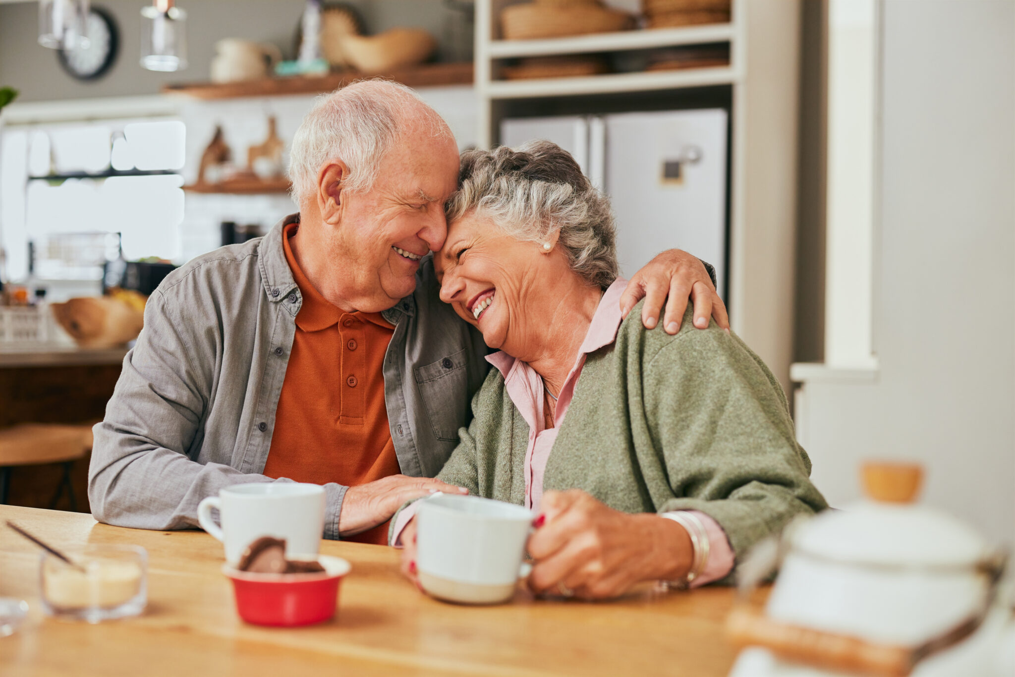 Elderly couple hugging while holding a cup of tea.