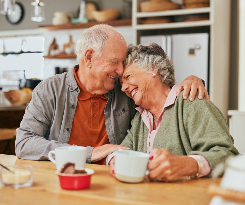 Elderly couple hugging while holding a cup of tea.