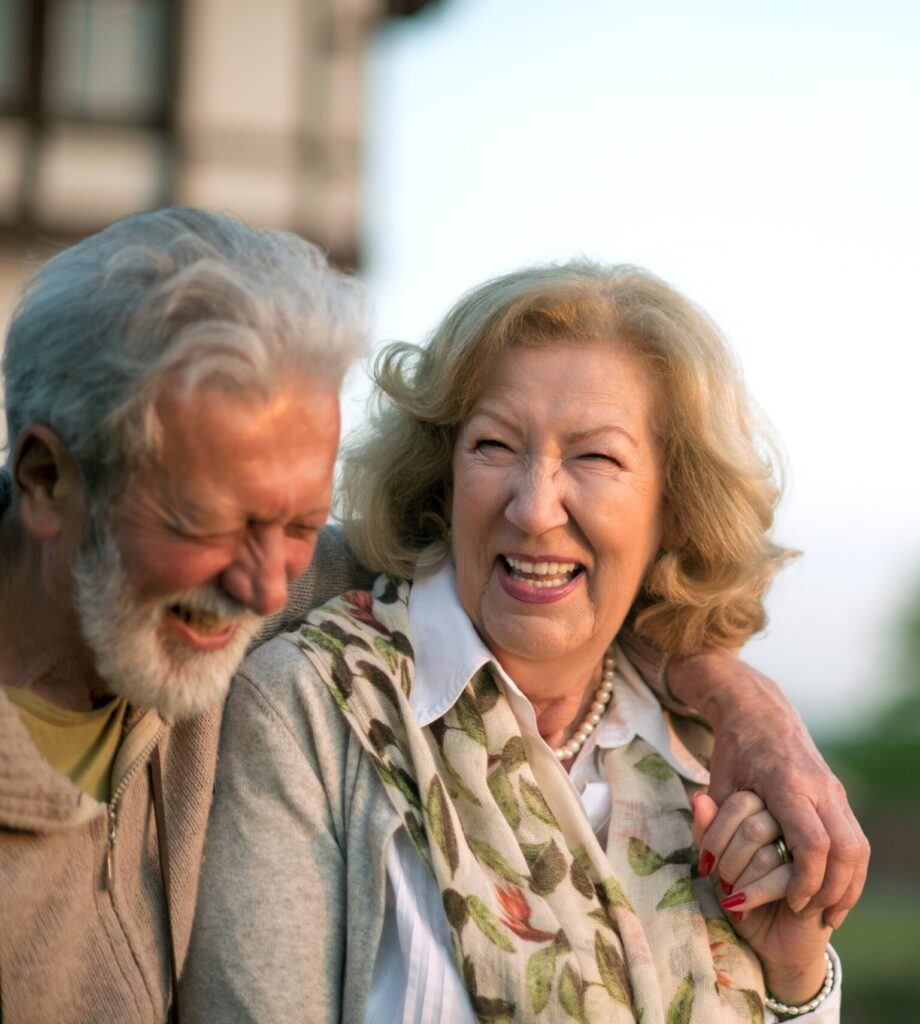Elderly couple laughing and holding each other outdoors.