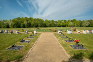 Path lined with memorial plots and flowers leading to a reed pond