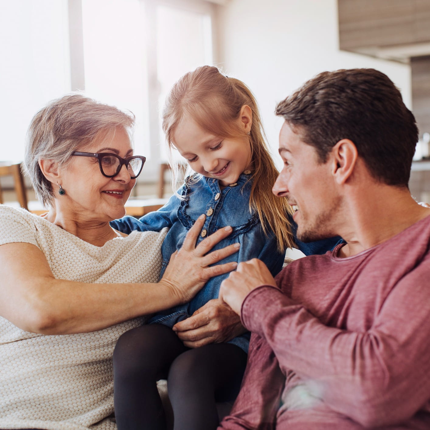 Grandmother, father, and granddaughter smiling together at home